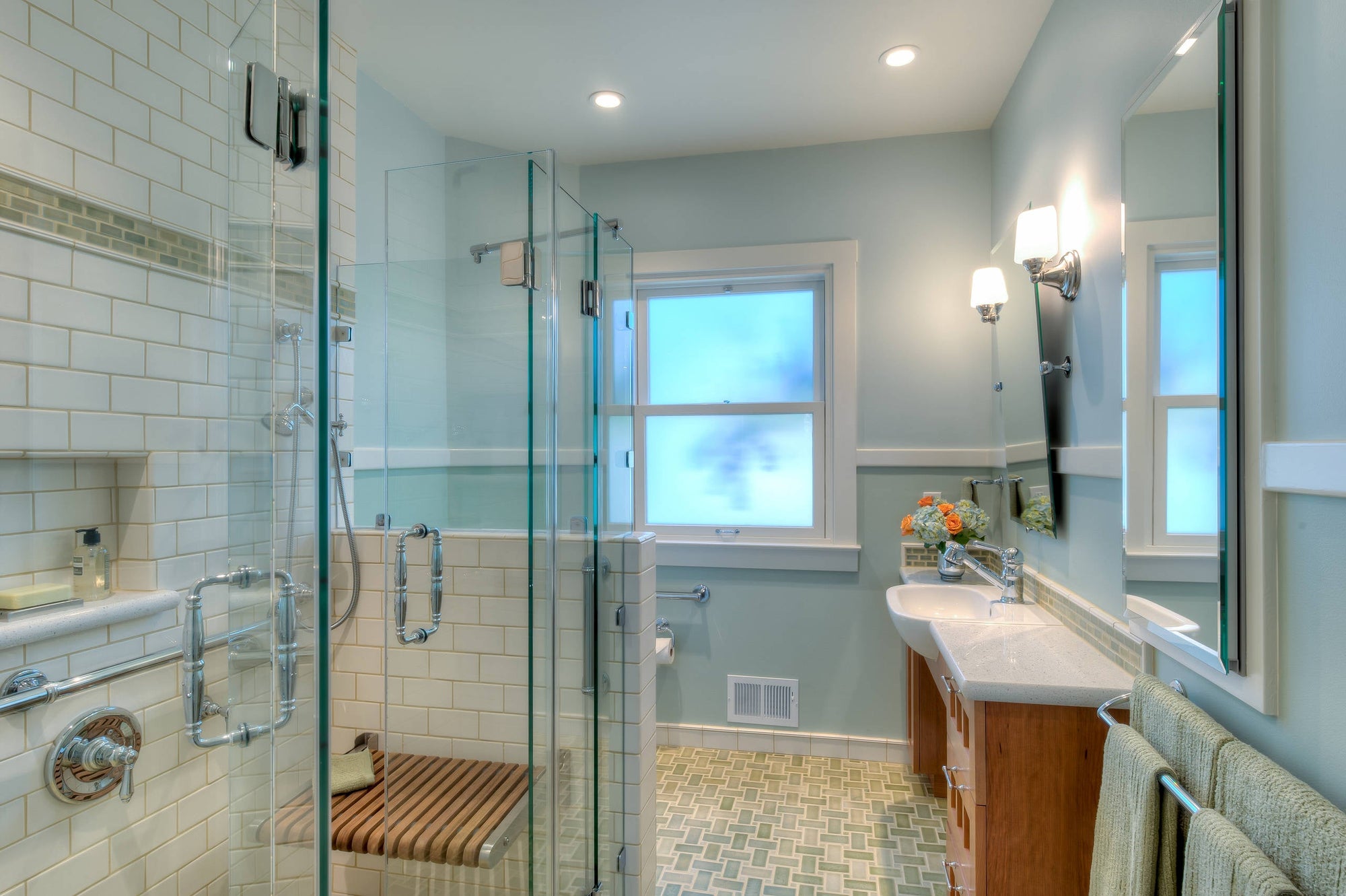 A bright, accessible bathroom featuring a glass bi-fold shower door, built-in bench, and modern vanity setup | ACE DECOR