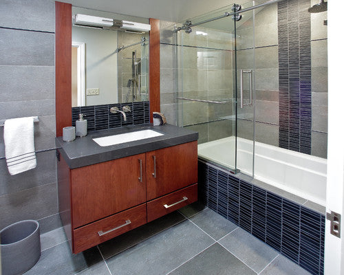 a modern bathroom featuring frameless bathtub shower doors with a sleek sliding mechanism, complemented by dark tiles and a stylish wooden vanity. | ACE DECOR