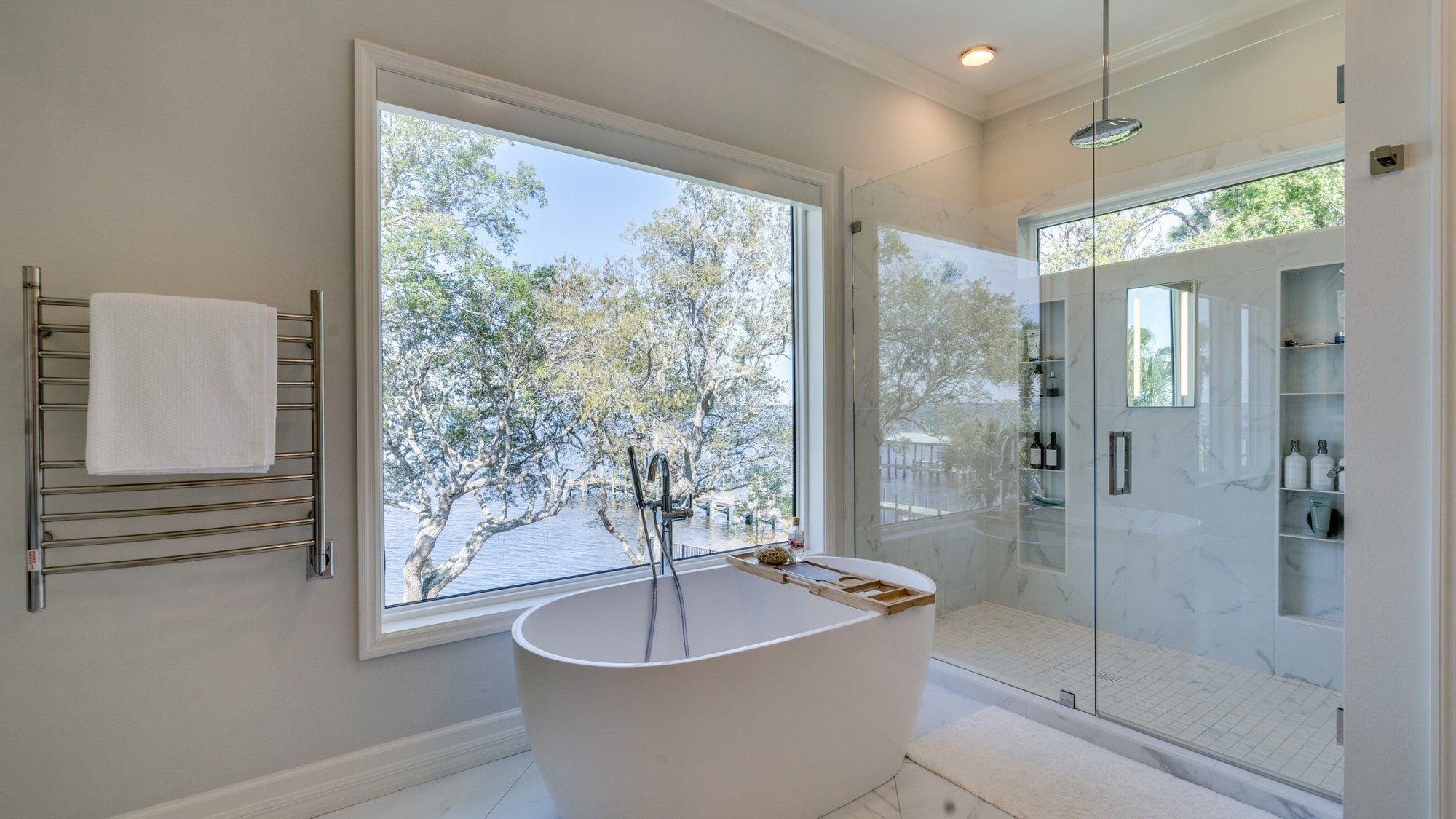 A luxurious bathroom featuring a freestanding bathtub deep soaking tub with a stunning lake view and a glass-enclosed shower. | ACE DECOR