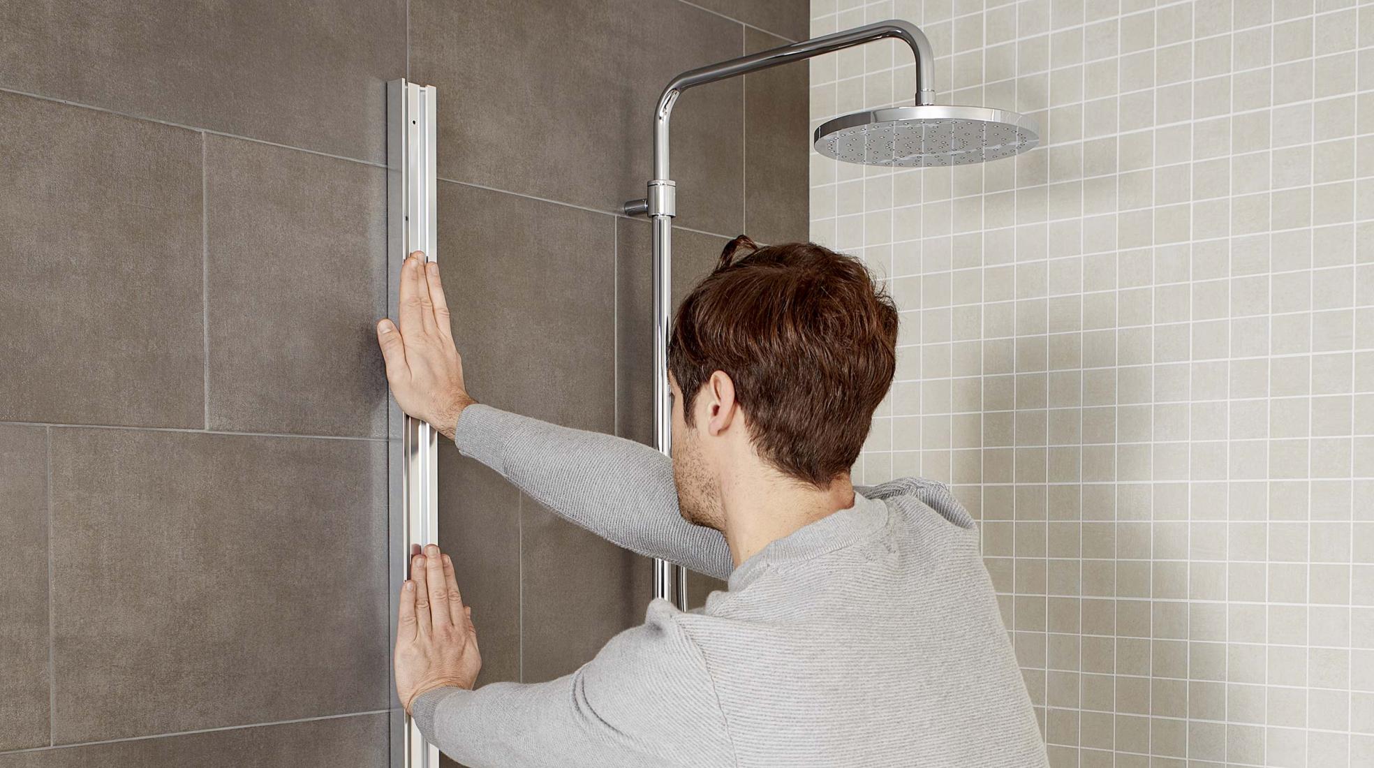A man installs an aluminum shower profile onto a tiled bathroom wall. | ACE DECOR