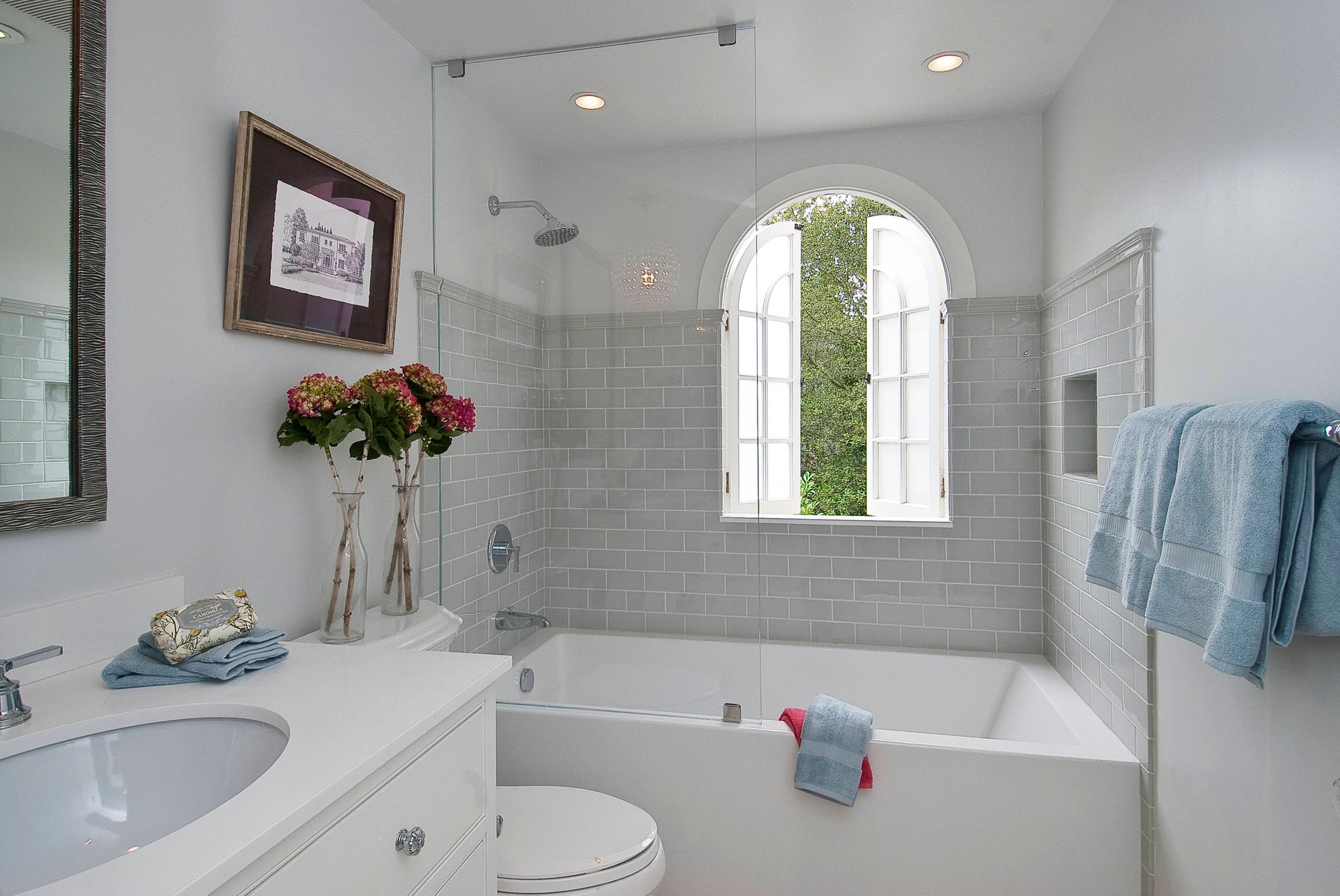 A bright and elegant bathroom featuring sleek frameless bathtub shower doors and soft blue towels. | ACE DECOR