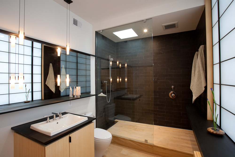 A modern, minimalist bathroom featuring a sleek walk-in shower with a full glass screen, black tile walls, and soft ambient lighting. | ACE DECOR
