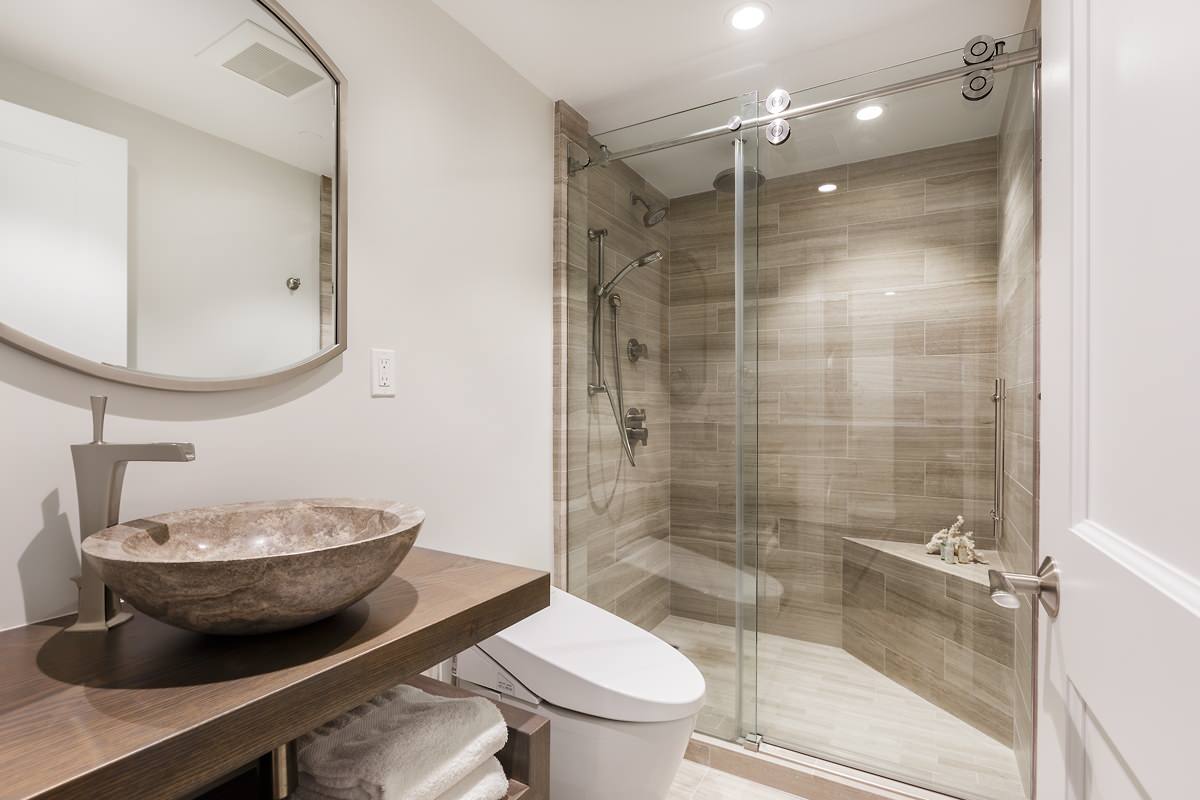 A modern bathroom featuring a vessel sink and frameless bypass shower doors enclosing a tiled shower area. |ACE DECOR