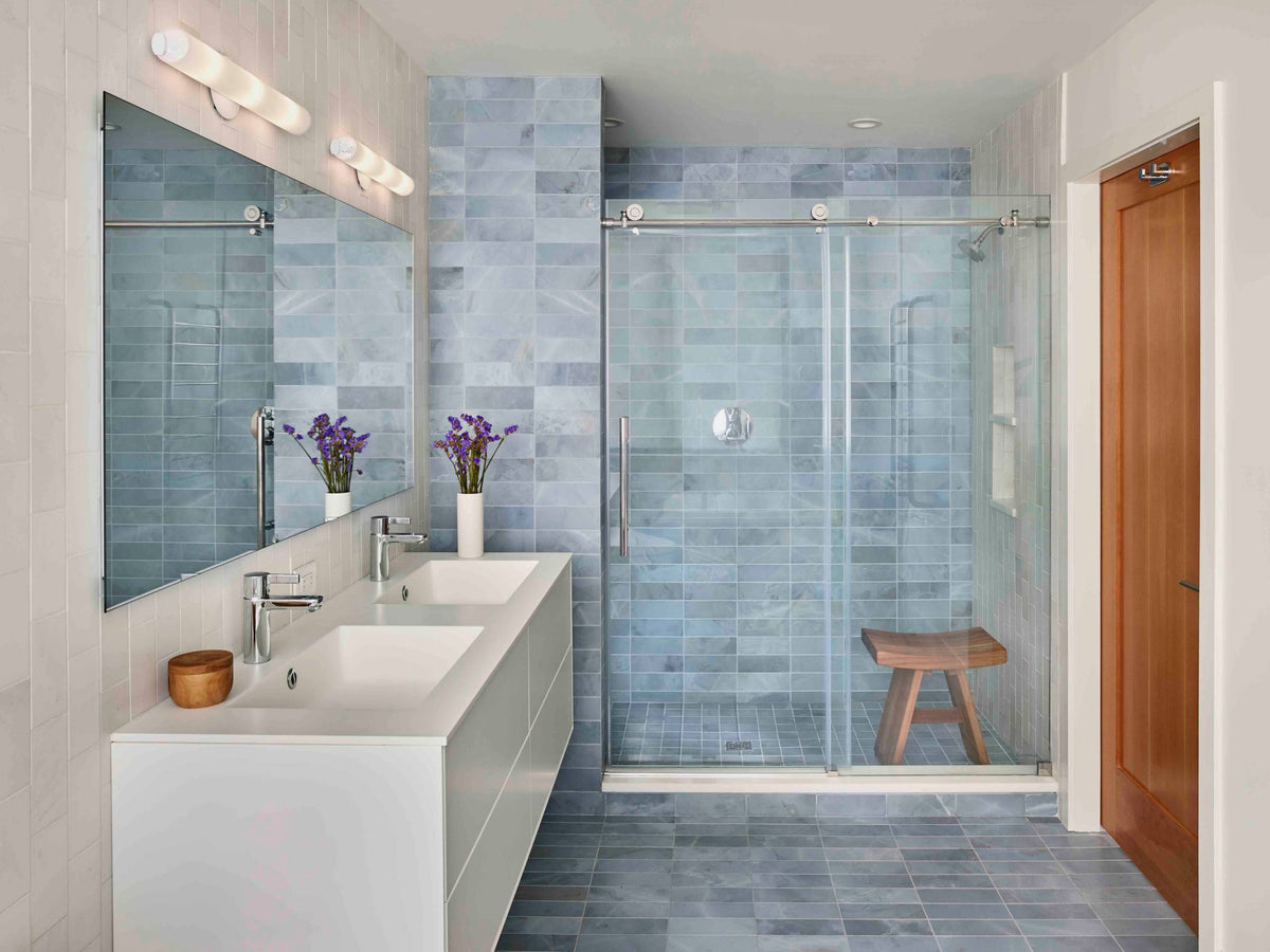A modern bathroom featuring a sleek glass shower sliding door, soft blue tile walls, and a minimalist double vanity with clean, contemporary lines. | ACE DECOR