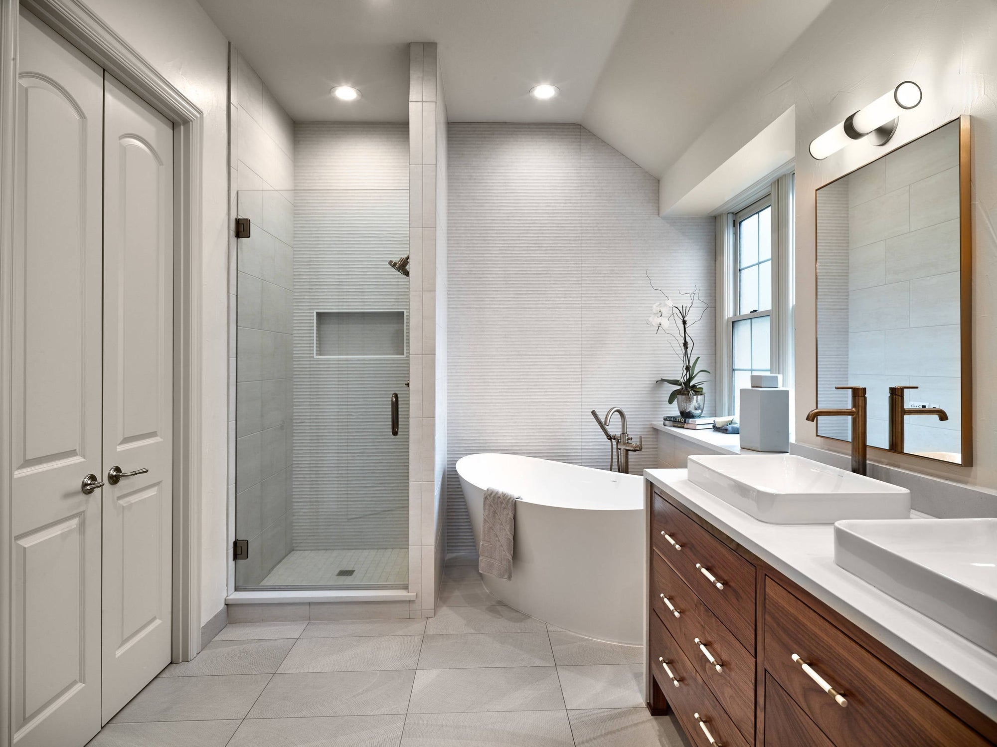 A modern bathroom with white tiles, an elegant freestanding tub, and two vanity sinks. | ACE DECOR