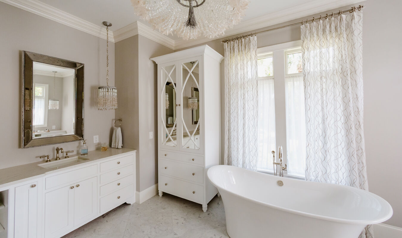 a stylish, modern bathroom with a freestanding bathtub, white cabinetry, elegant mirrors, and large windows allowing natural light to flood the space. | ACE DECOR