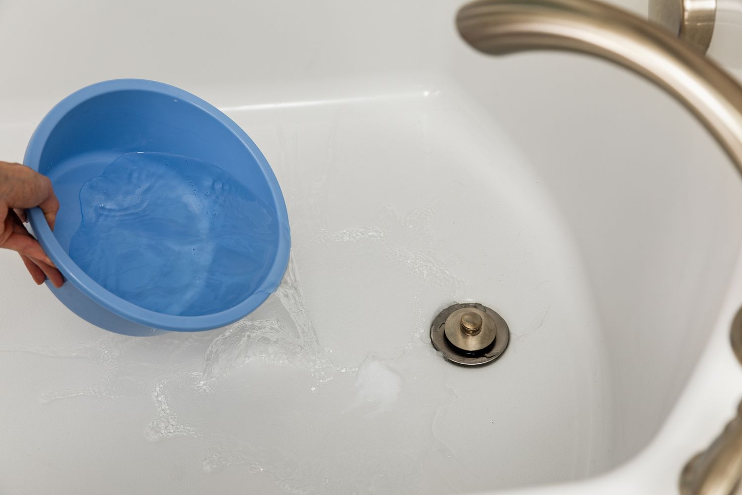A person pouring water into a clean white bathtub using a blue basin. | ACE DECOR