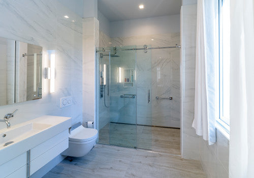 a bright, modern bathroom featuring frameless sliding glass shower doors, marble-style walls, a floating vanity, and a sleek wall-mounted toilet for a clean, minimalist aesthetic. | ACE DECOR