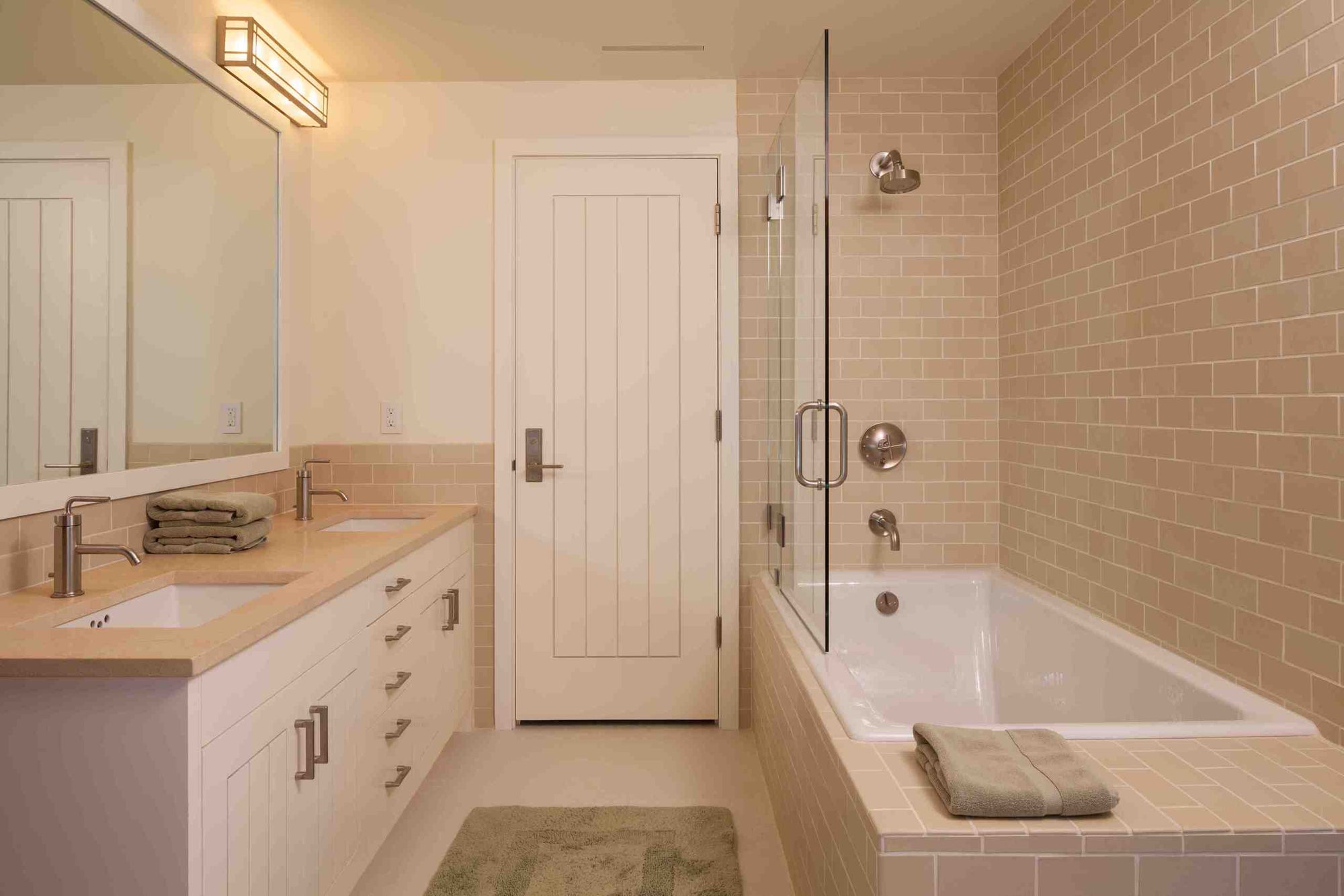 Contemporary bathroom featuring a frameless glass tub door, dual-sink vanity, and warm beige tile. | ACE DECOR