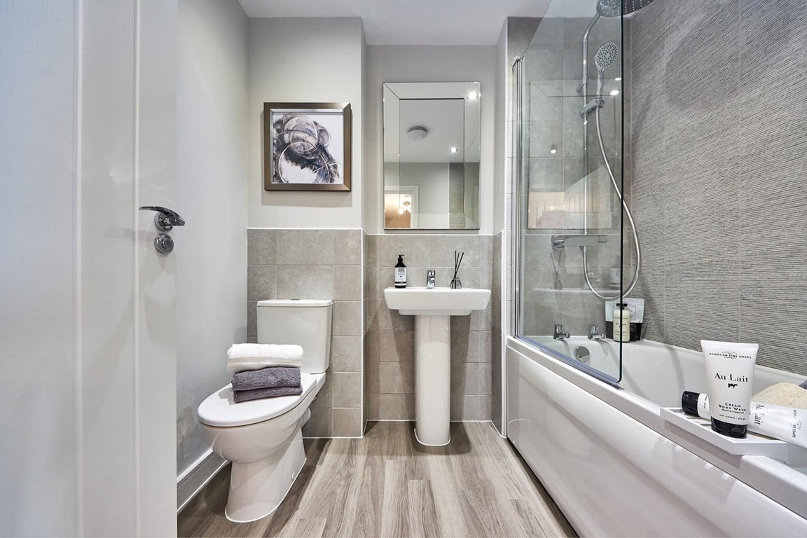 Modern bathroom featuring shower doors on the bathtub, a sleek pedestal sink, and neutral-toned decor. | ACE DECOR