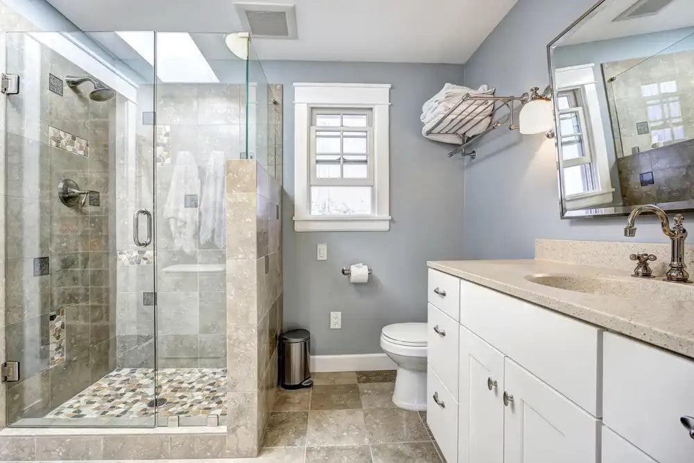 Elegant compact bathroom featuring frameless sliding shower glass doors and mosaic tile floor