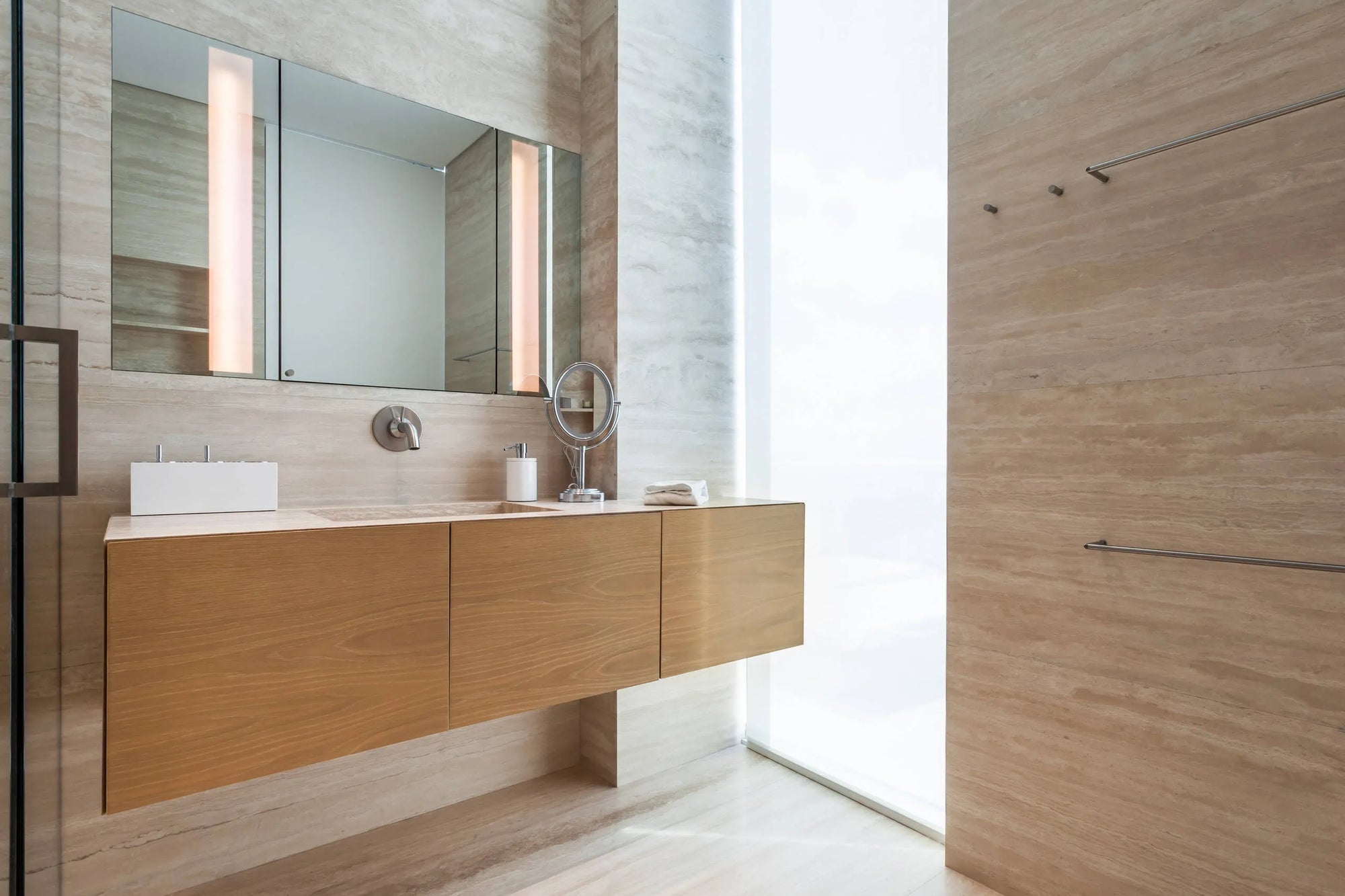 Modern bathroom with light-wood floating vanity, large mirror, and natural light from window. Sleek minimalist design.