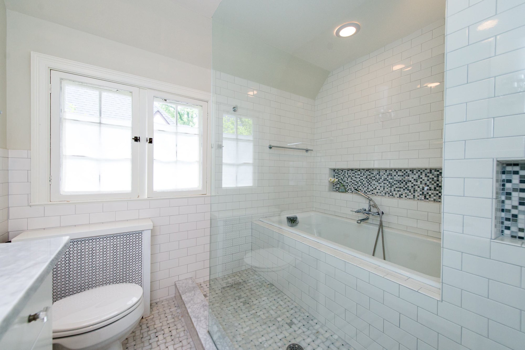 Modern bathroom featuring a sleek glass shower enclosure with tub, accented by white subway tiles and mosaic detailing. | ACE DECOR