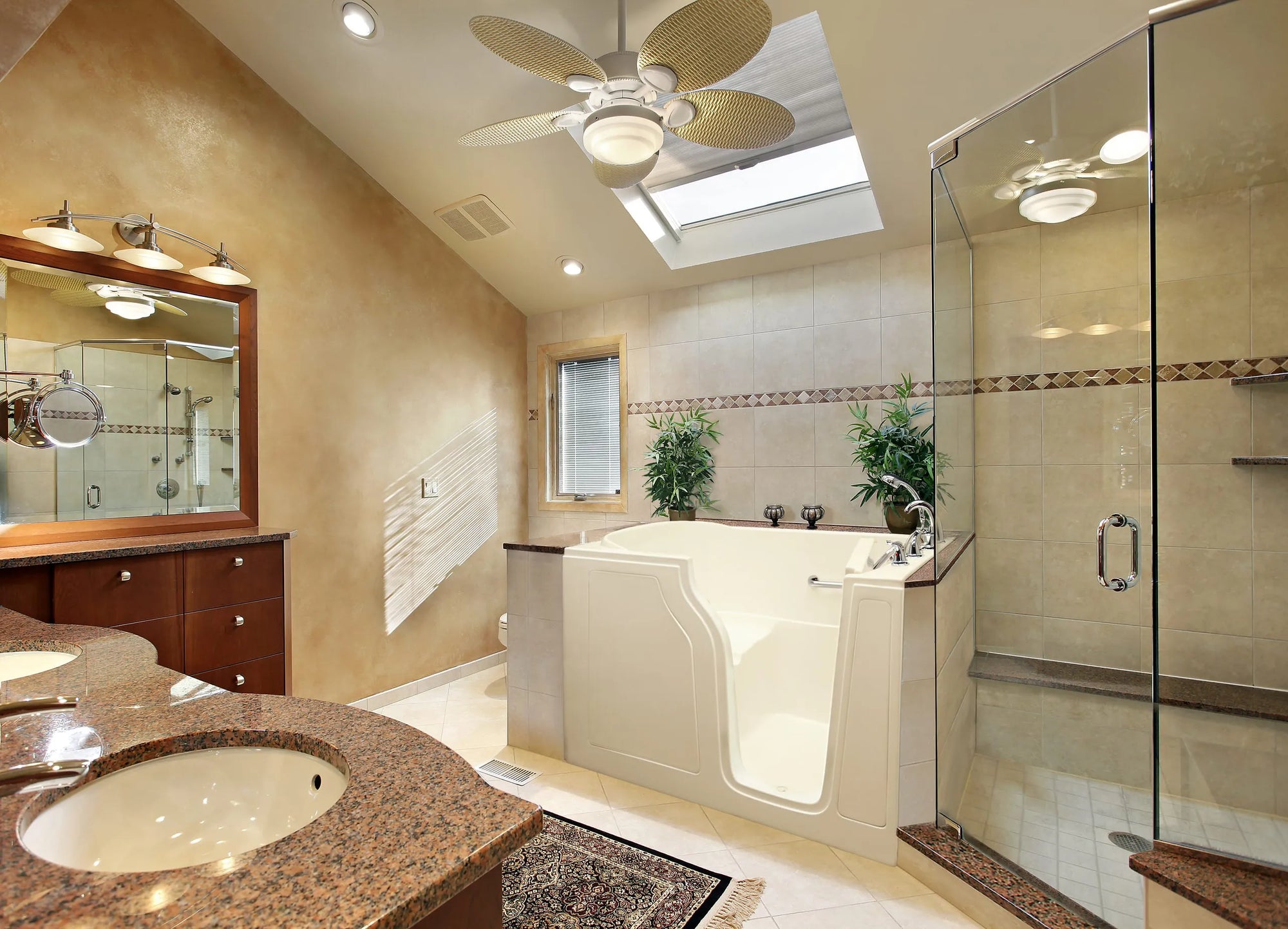 Luxurious bathroom with white walk-in bathtub, double sinks, glass shower, natural light from skylight, and decorative plants.
