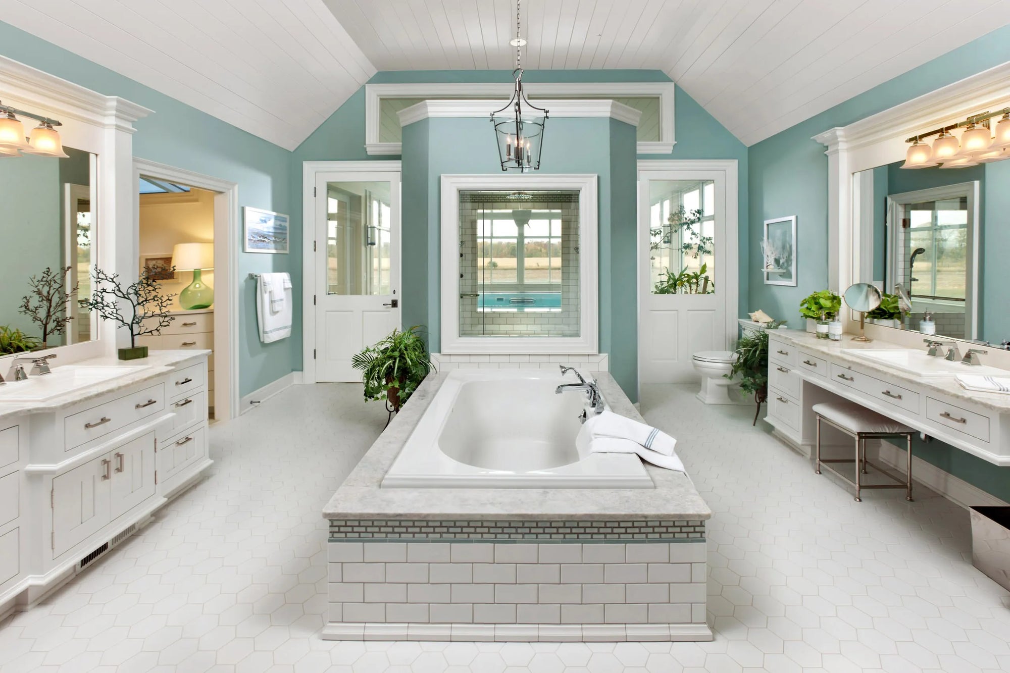 Luxurious bathroom with drop-in bathtub, white tiles, light blue walls, potted plants, and chandelier.