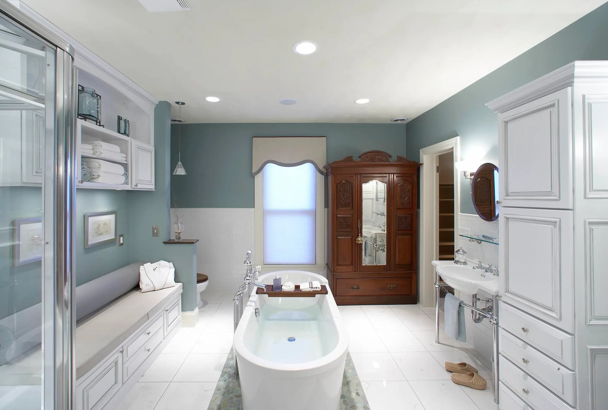 Spacious light blue and white bathroom with freestanding bathtub featuring a wooden bathtub tray caddy holding toiletries, natural light, serene décor.