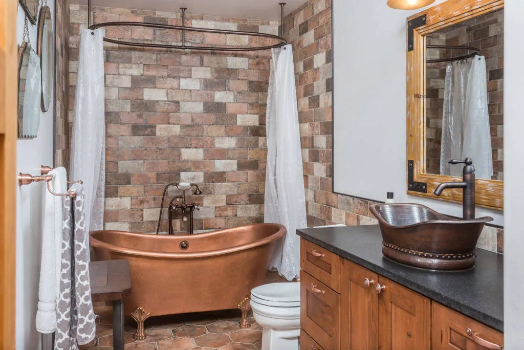 Vintage copper bathtub with elegant white curtains in a brick-walled bathroom.