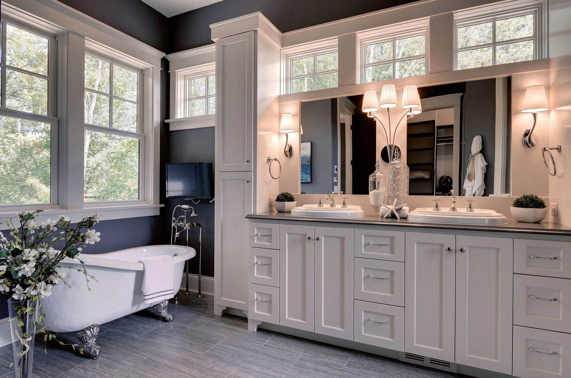 Vintage enameled steel bathtub near large window with natural light, dark gray walls, and double vanity in modern bathroom design.
