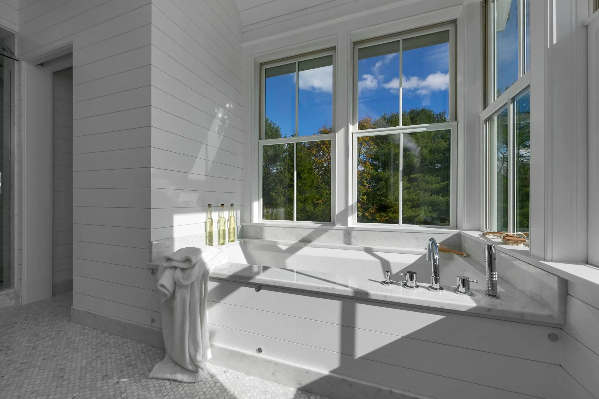 Modern tub faucet in serene bathroom with expansive windows and lush greenery views.