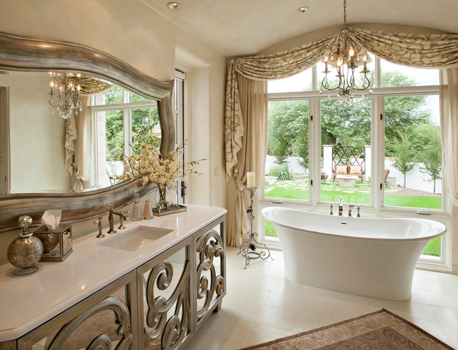 A luxurious bathroom featuring a grand soaking bathtub, elegant double sink vanity with ornate silver accents and floor-to-ceiling windows