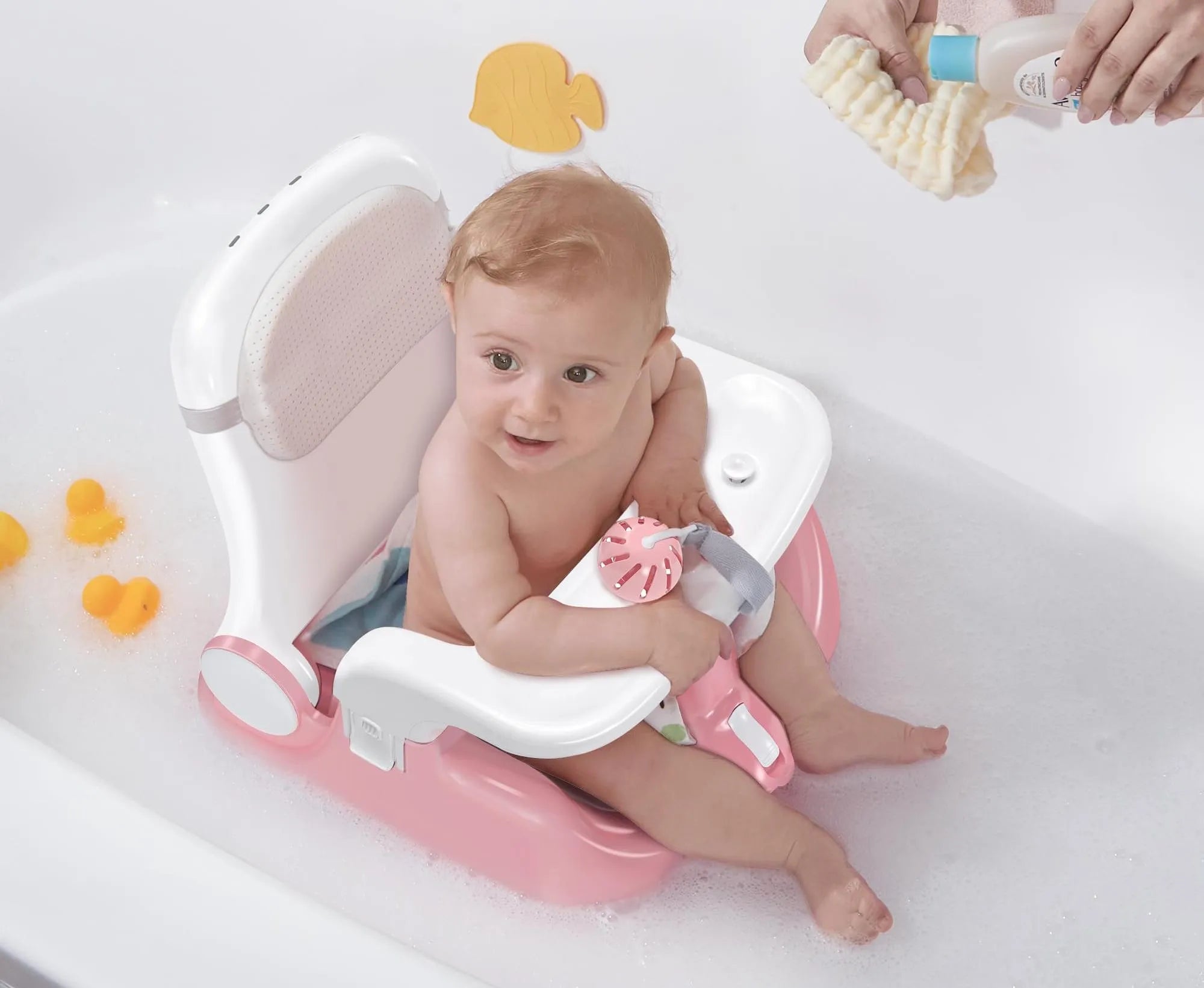 Pink and white infant bathtub seat with supportive backrest, baby holding bath toy amid soapy water and floating rubber duckies during safe bathing.