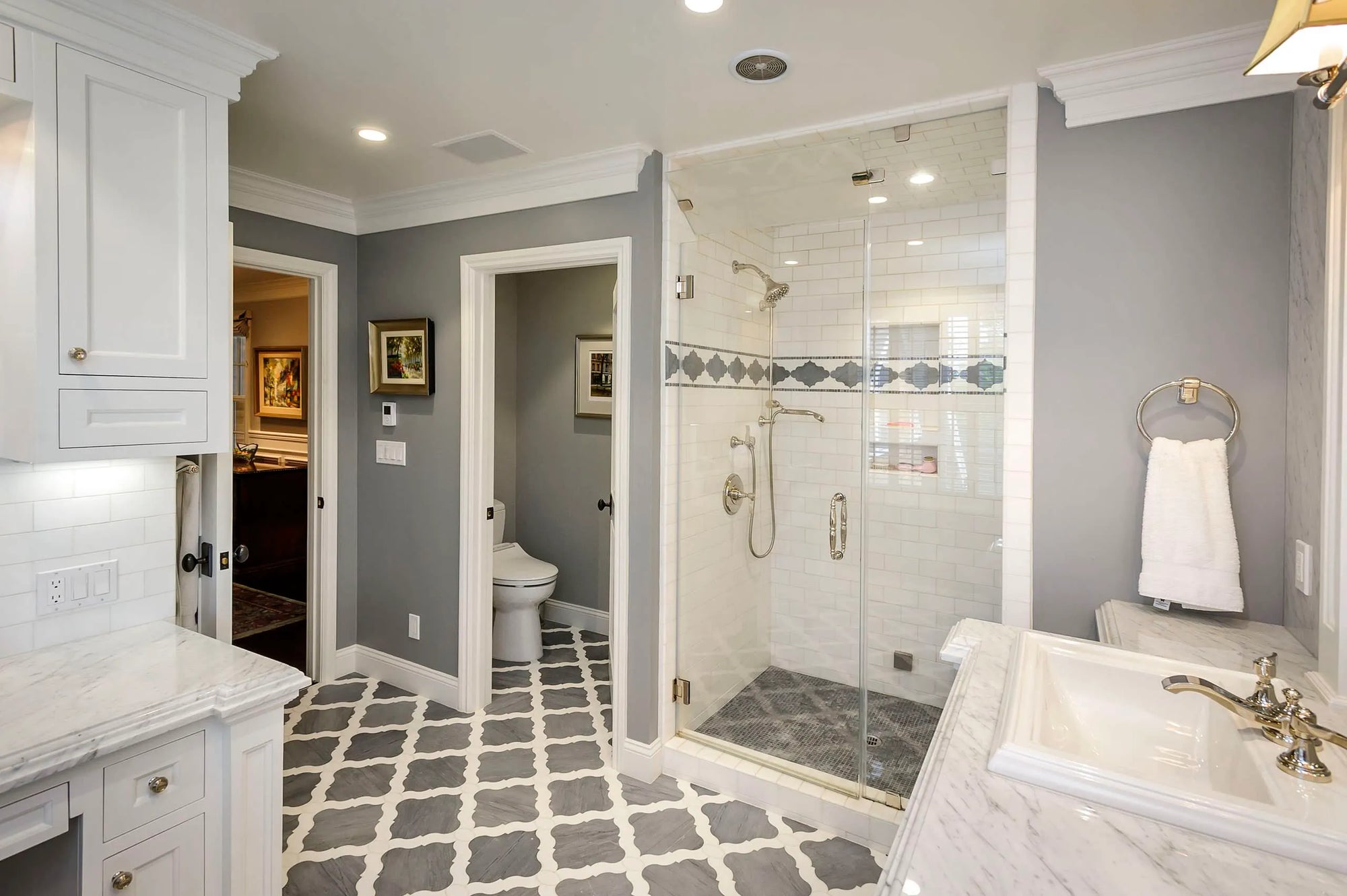 Modern gray and white bathroom featuring glass-enclosed shower, marble vanity, geometric tile flooring, and smart toilet in background.