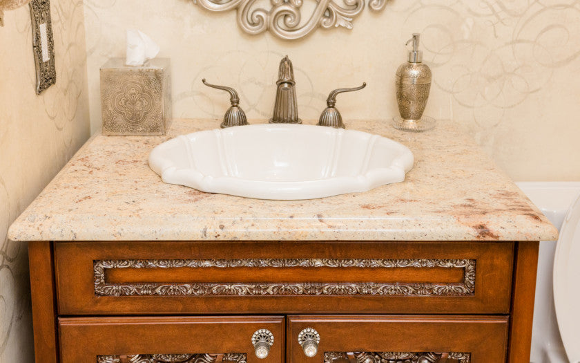 Traditional style granite top bathroom vanities with ornate wood detailing and scalloped sink.