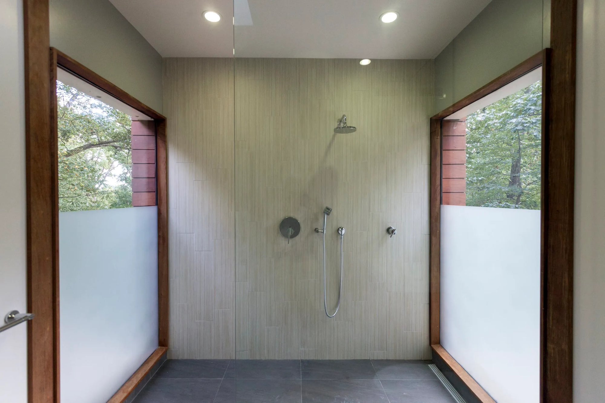 Modern 3-way shower system in minimalist bathroom with wood backdrop, frosted glass panels, and recessed lighting.