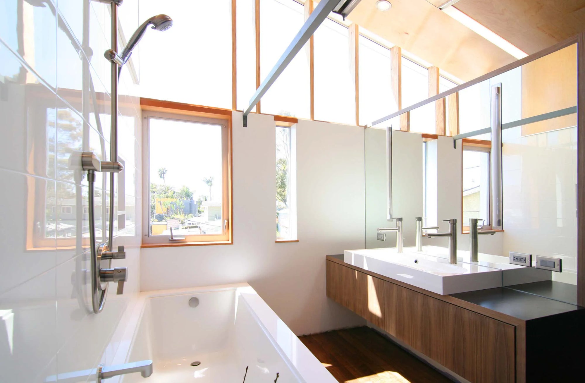 White alcove bathtub against large windows in bright modern bathroom with wood accents and minimalist design.​