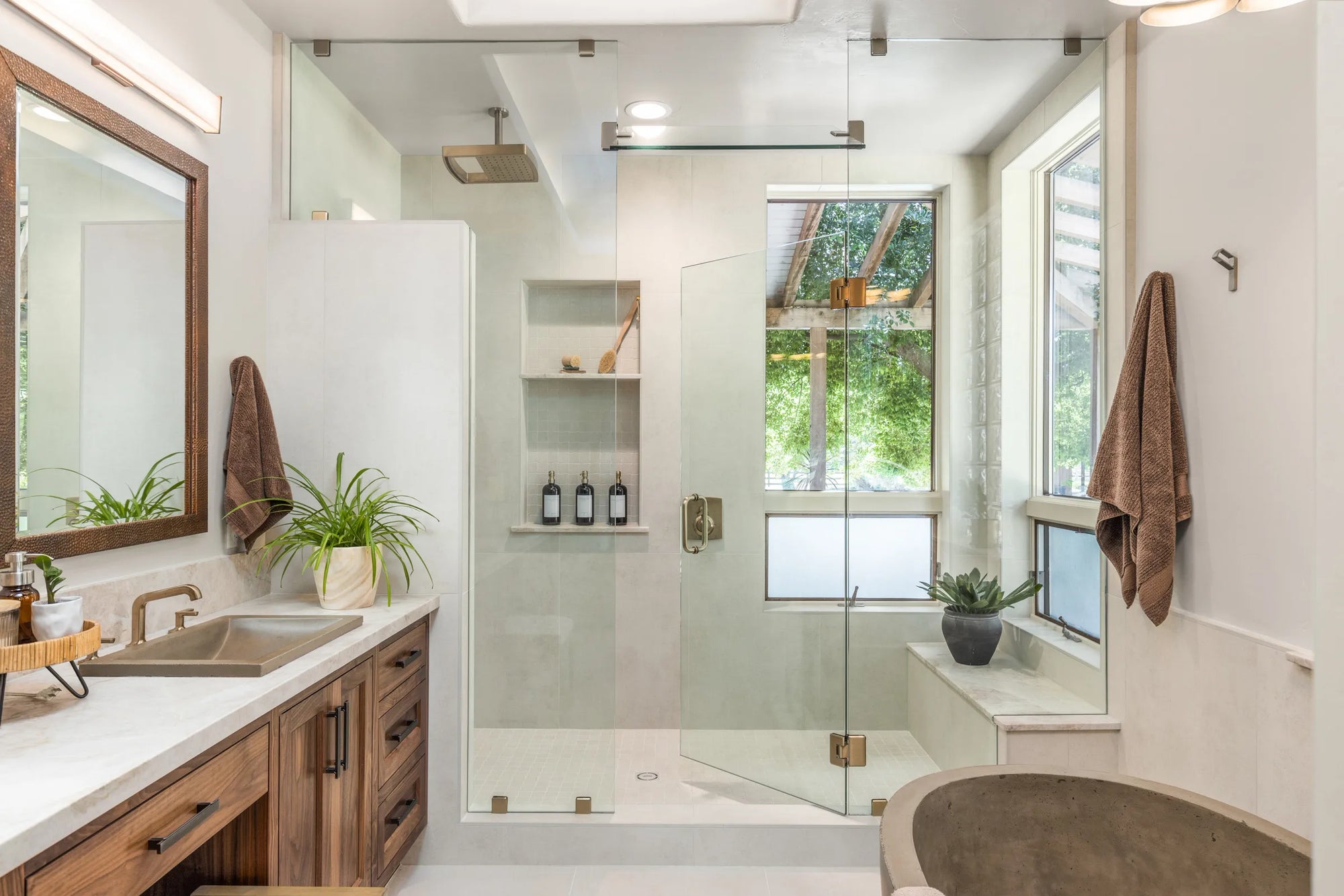 Glass shower door in minimalist bathroom with greenery & freestanding tub.