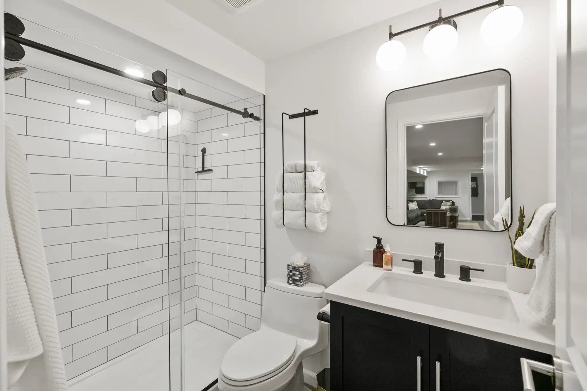 Modern bathroom with frameless sliding door shower, white subway tiles, black fixtures, vanity, and toilet. Minimalist black & white design.​