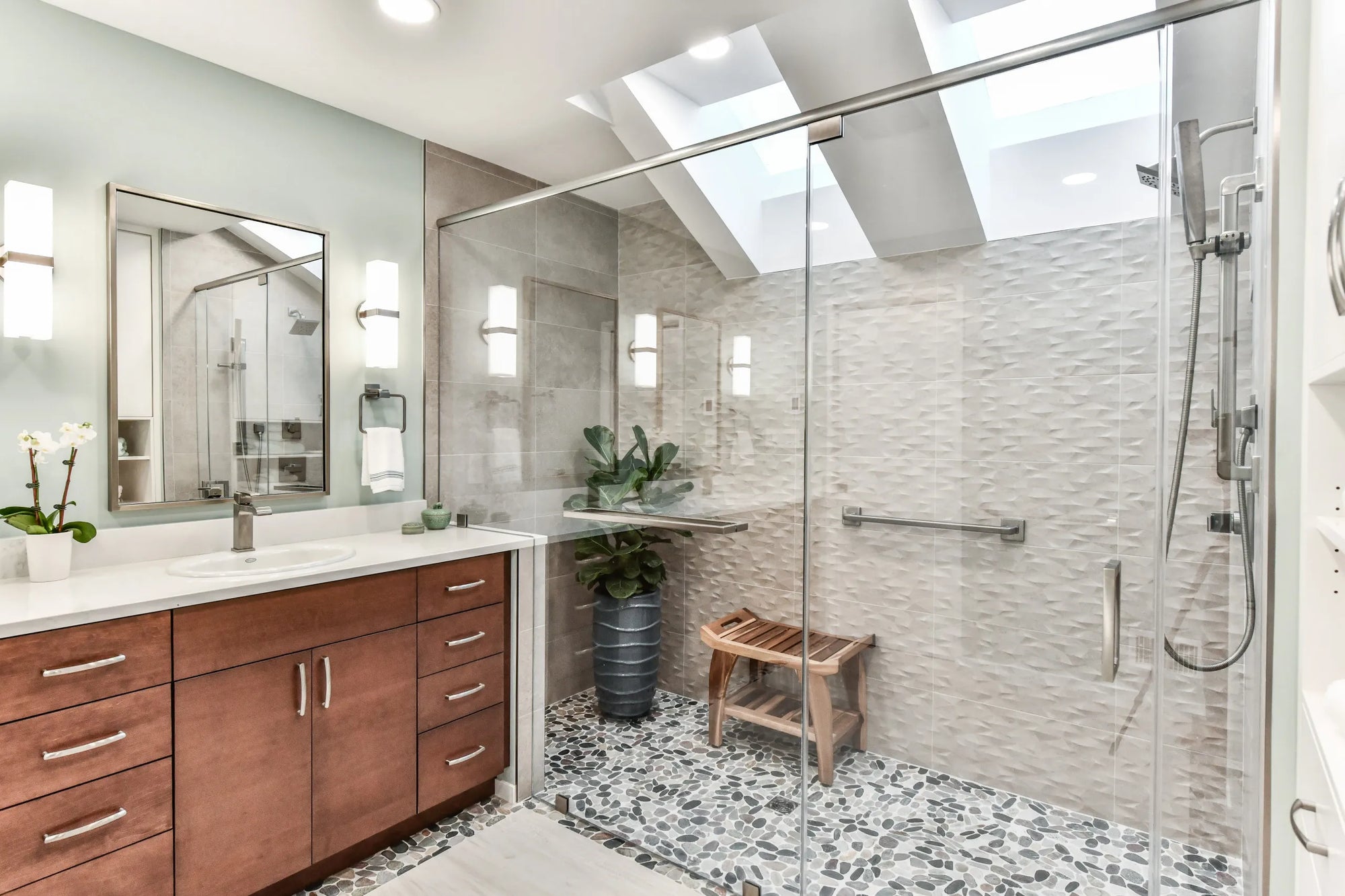 Modern bathroom with spacious walk-in shower featuring a sleek glass shower door, skylight, and wooden vanity.
