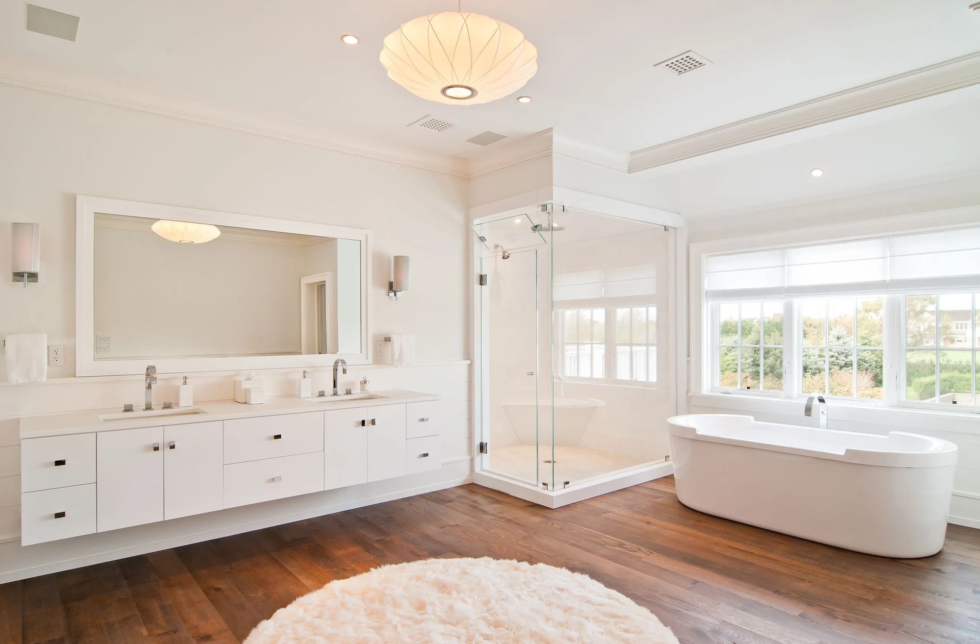 Modern glass shower door in spa-like bathroom with freestanding tub and bright natural lighting.