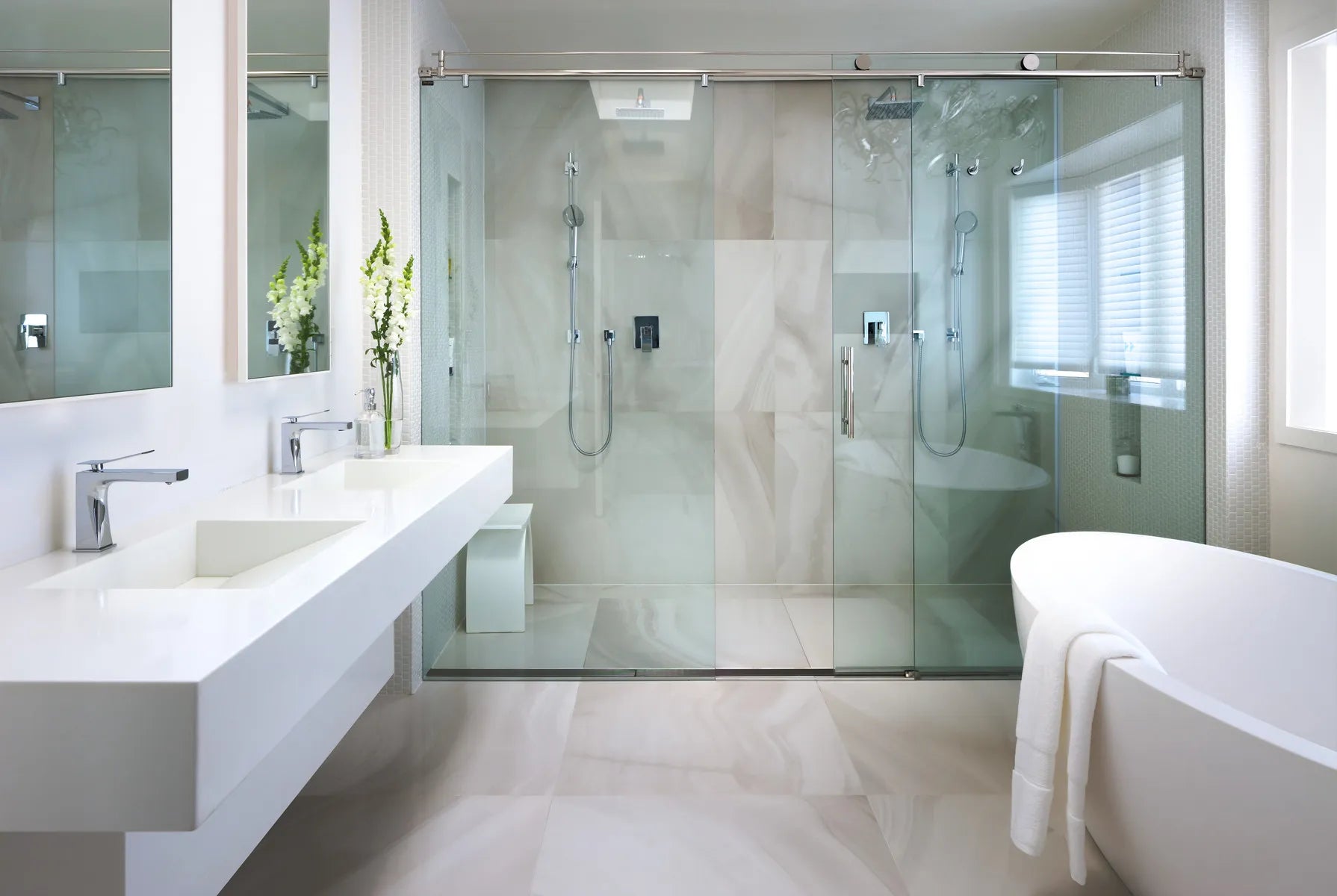 Modern bathroom with frameless glass shower door, freestanding bathtub, floating double vanity, marble tiles, and neutral luxury design.