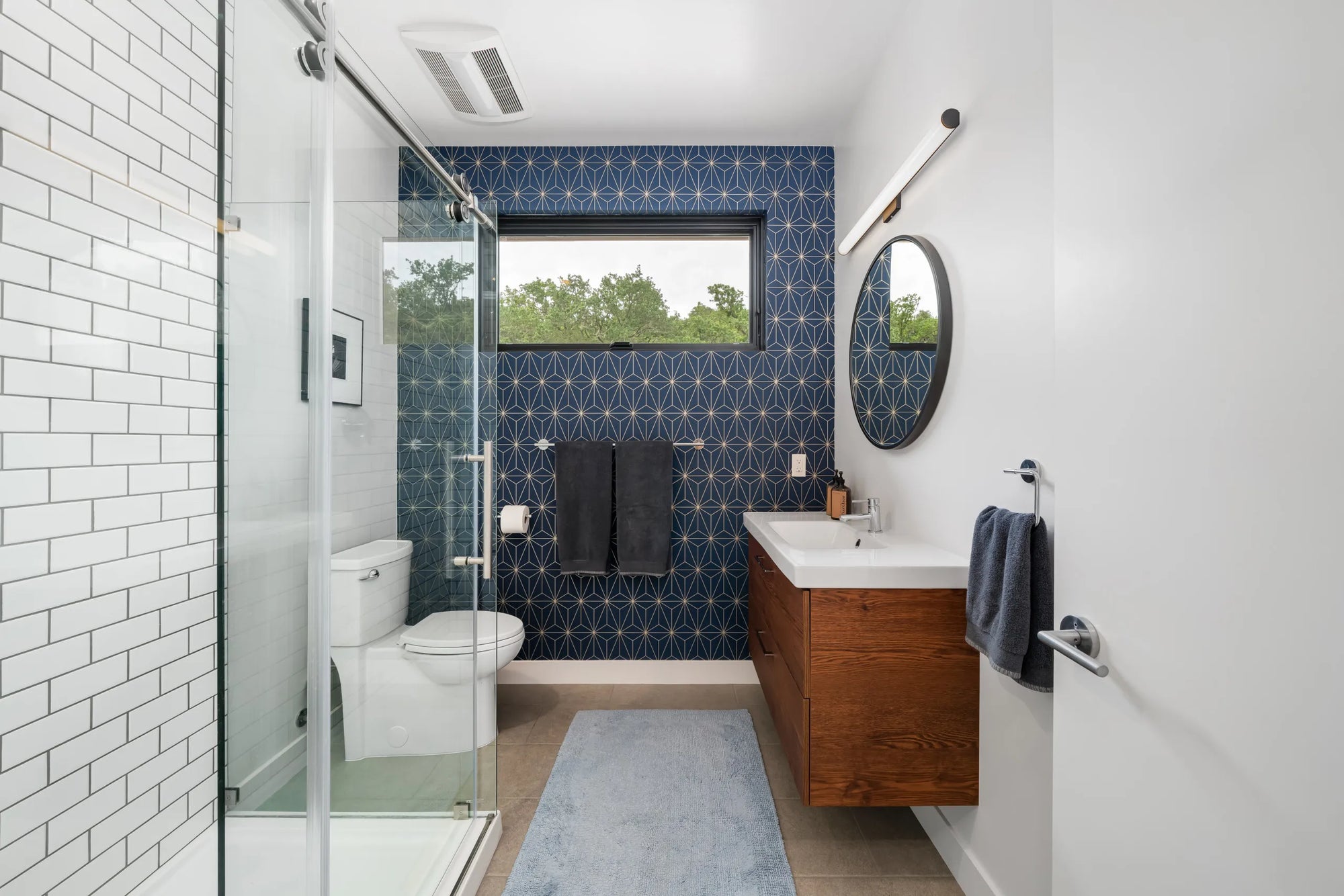 Frameless shower door in modern minimalist bathroom with white tiles and dark blue accent wall.​