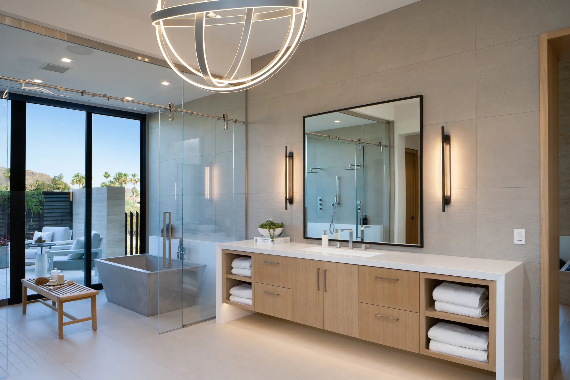 Frameless shower door in bright modern bathroom with freestanding bathtub and vanity under recessed lighting.​