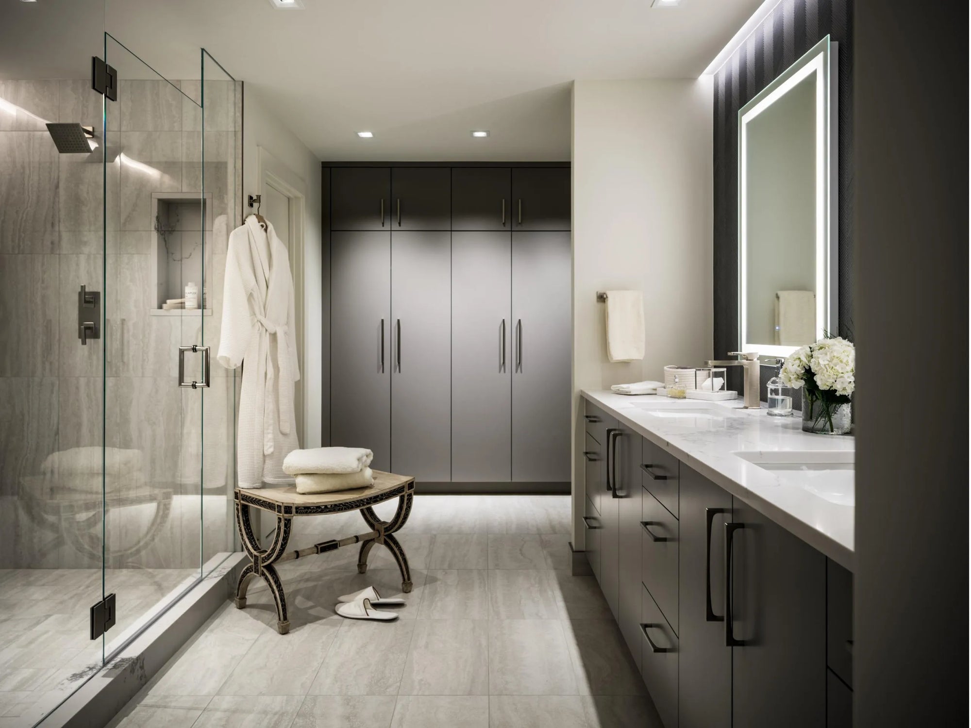 Glass hinge shower door in luxury bathroom with rainfall shower, vanity & bathrobe.