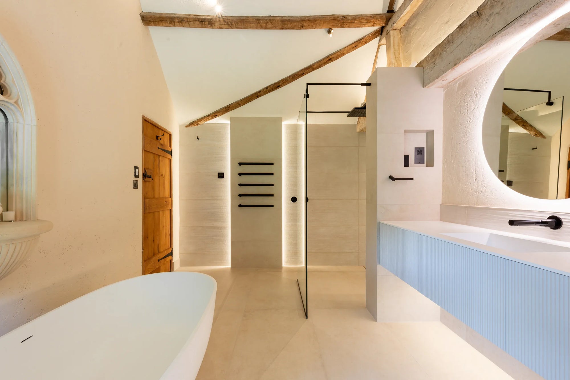 Modern Bathroom with Clear Frameless Shower Door, Freestanding Tub & Blue Vanity. Light Walls, Tiled Floor & Beamed Ceiling.​
