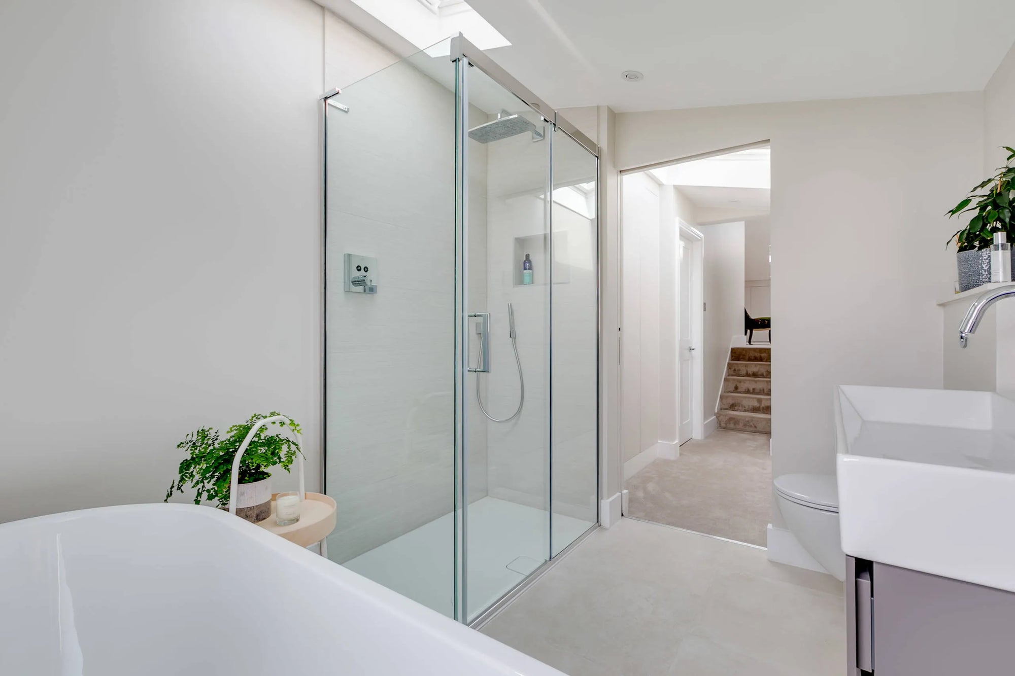 Modern minimalist bathroom featuring a clear glass walk-in shower door, freestanding bathtub, and natural accents.​