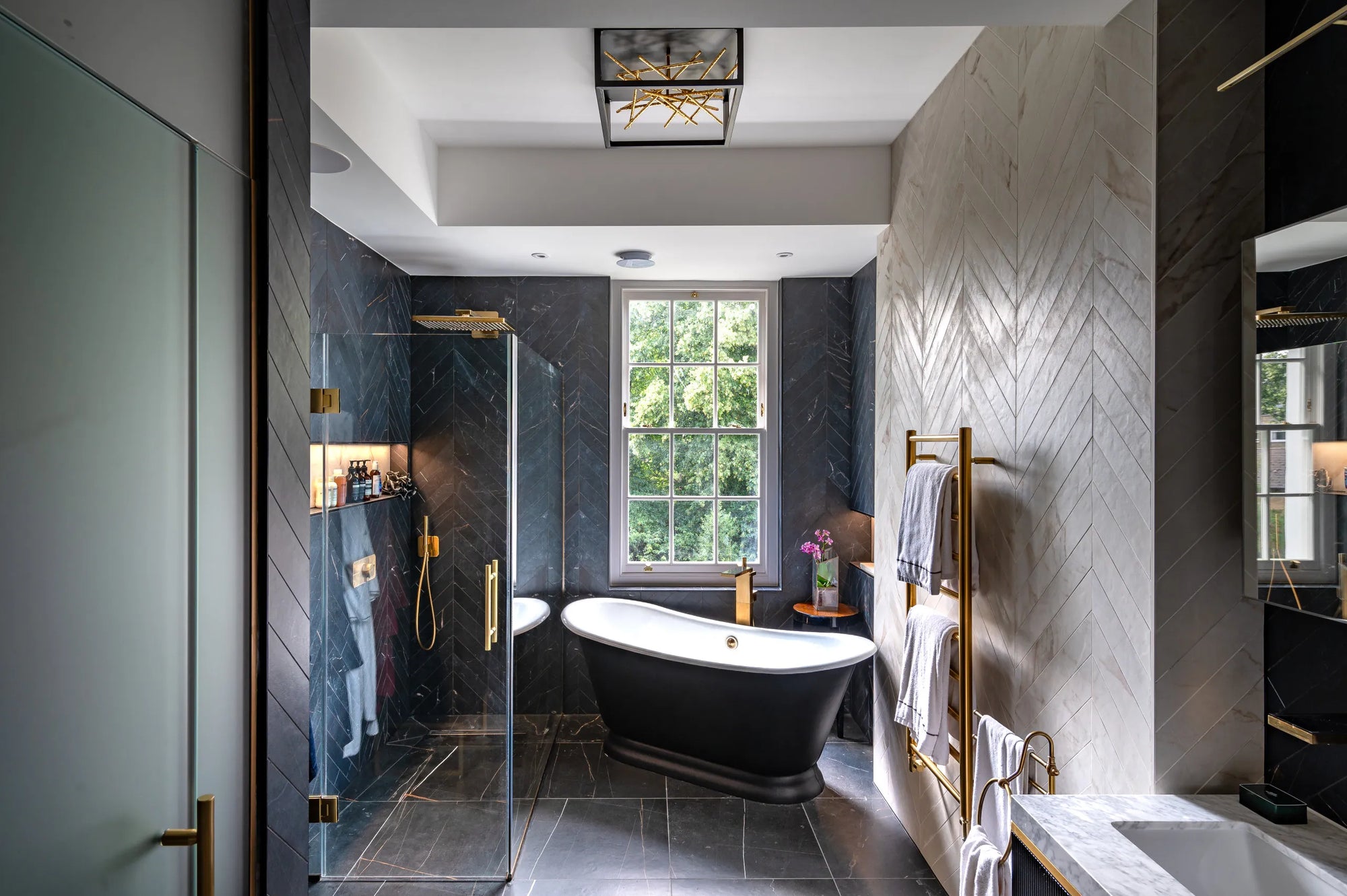 Luxury bathroom with gold-accented glass shower door, freestanding black bathtub, and dark herringbone tile accents.