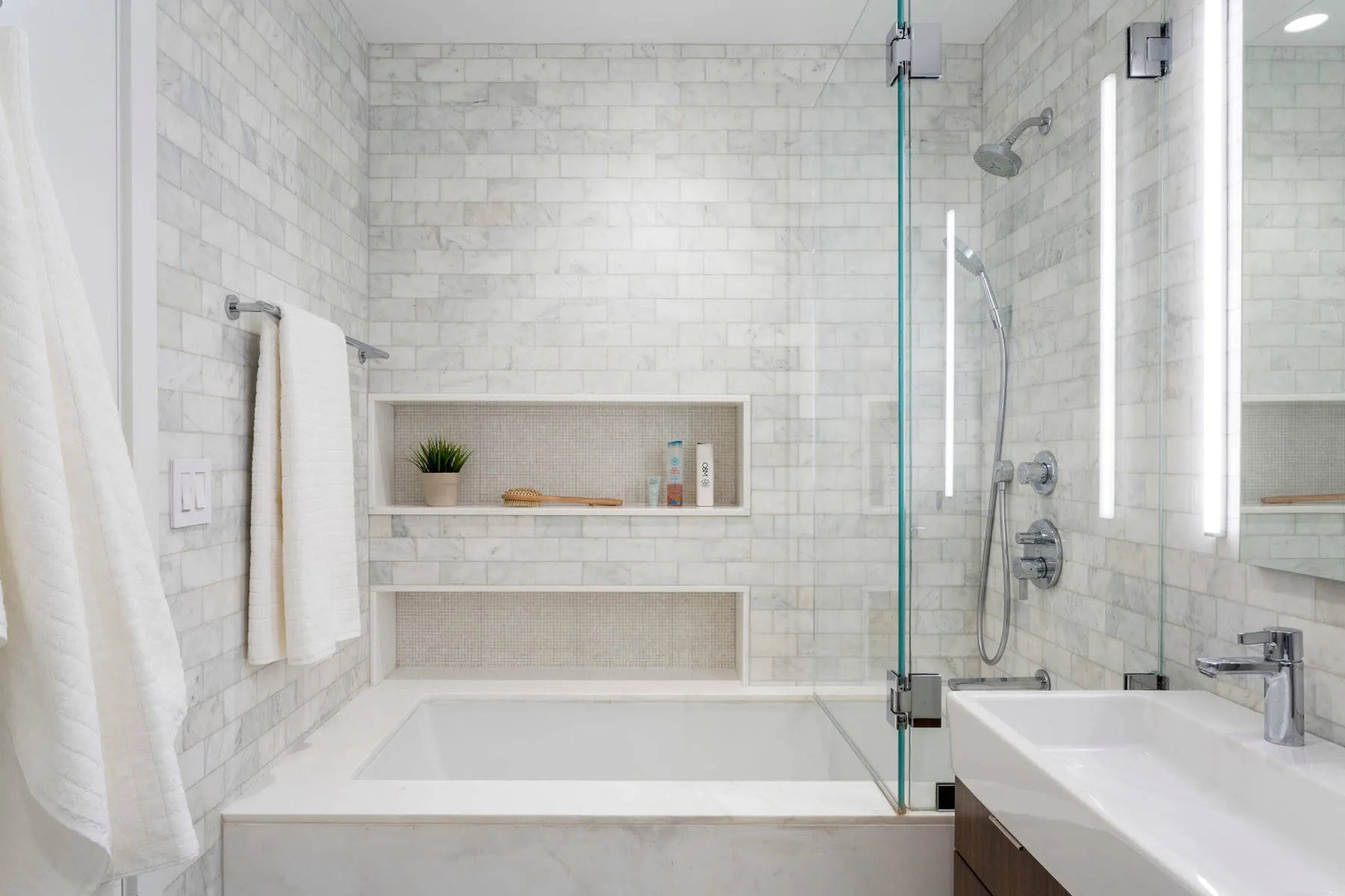 Modern bathroom with white alcove tub, marble tiles, recessed niches, and glass shower enclosure for spa-like luxury.