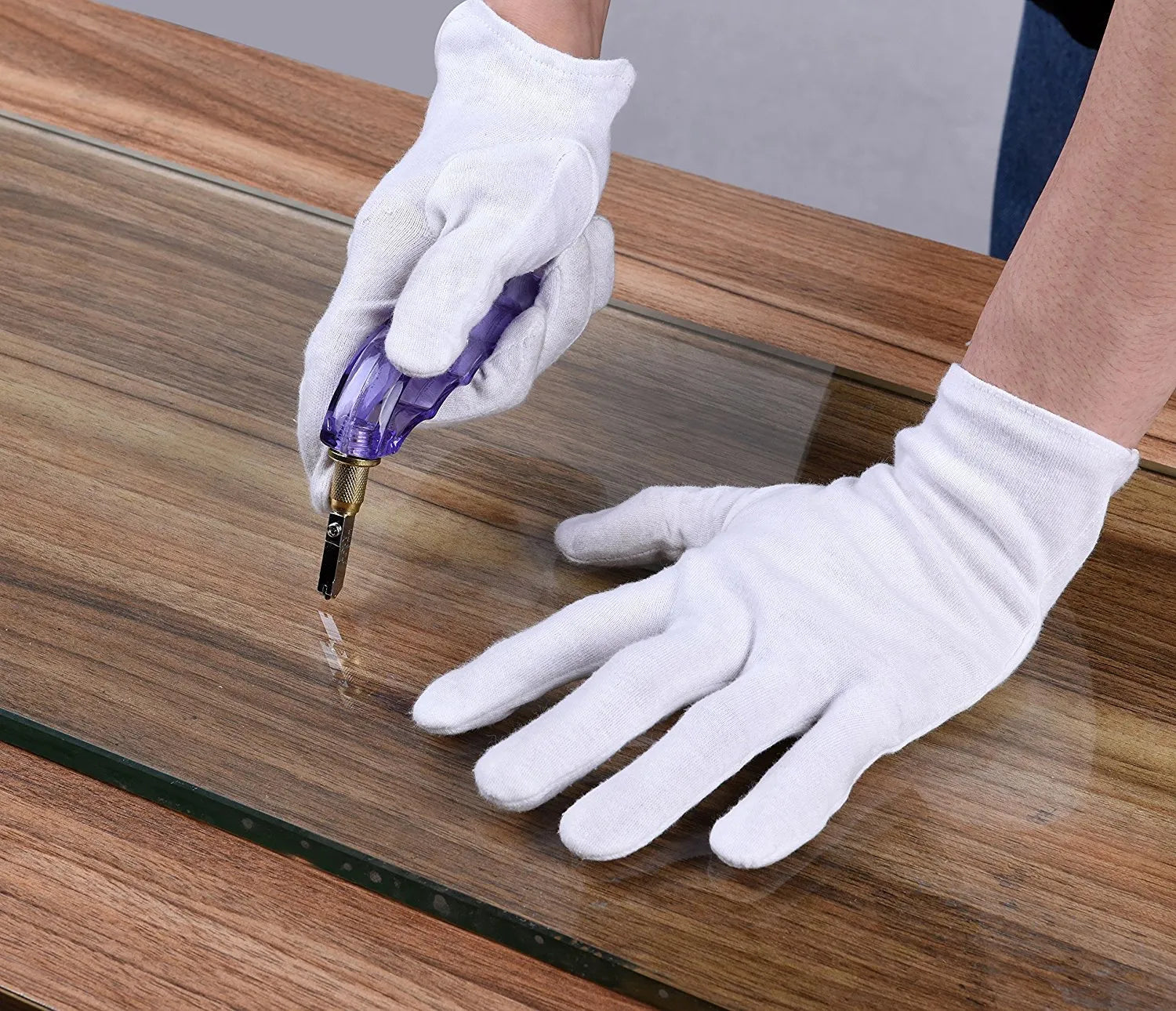 Professionals cut the mirror using a specialized cutting wheel tool with plastic handle on wooden surface.
