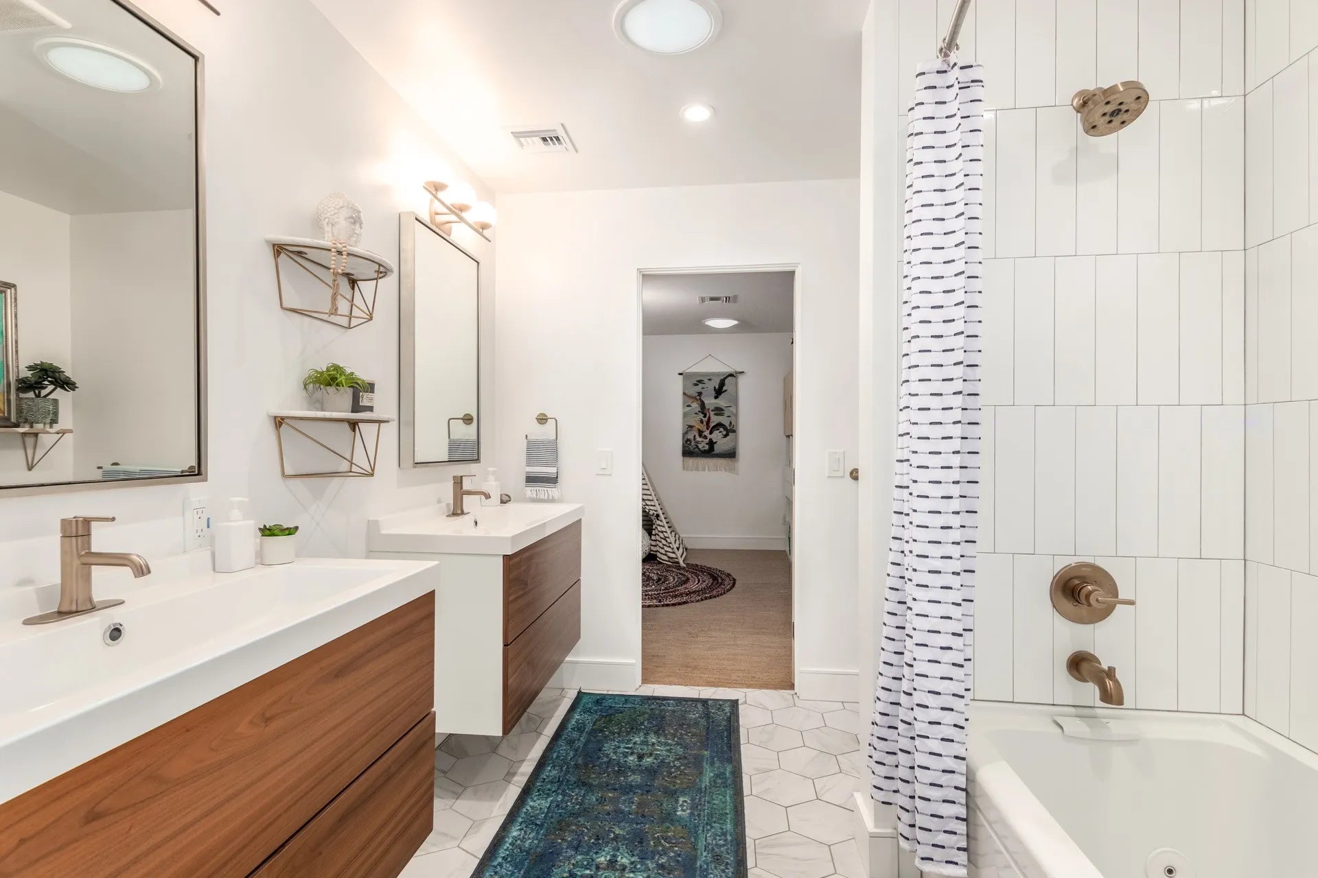 Modern Jack and Jill bathroom with dual vanities, bathtub, blue runner on white hex tiles, connecting two bedrooms.