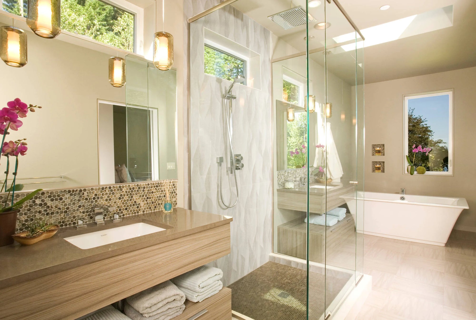 Modern bathroom glass shower with shower head and handheld wand, marble tile walls under natural skylight lighting.