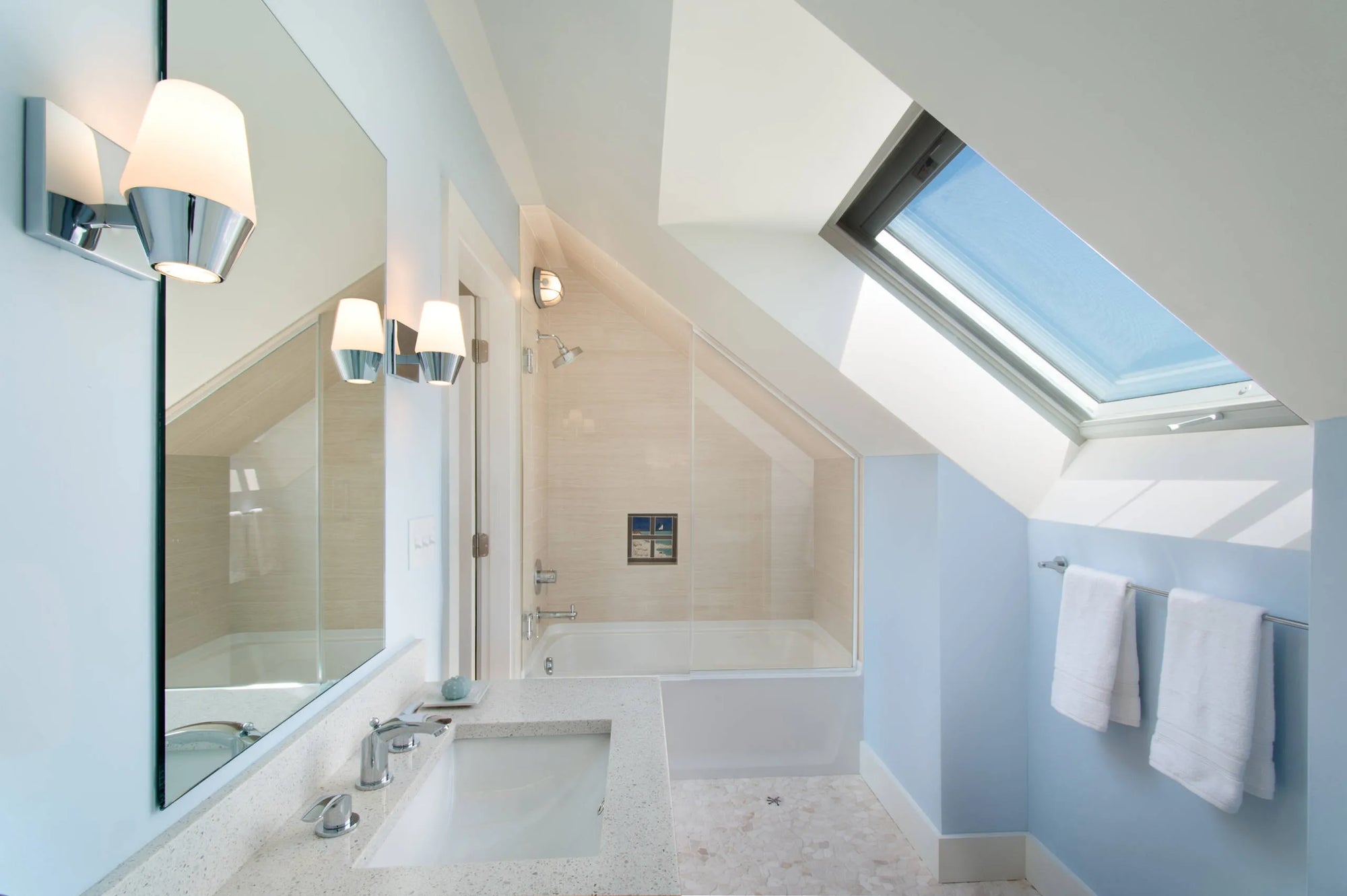 Modern minimalist bathroom featuring a bathtub shower combo with glass enclosure, dual-sink vanity, and skylight providing natural light.