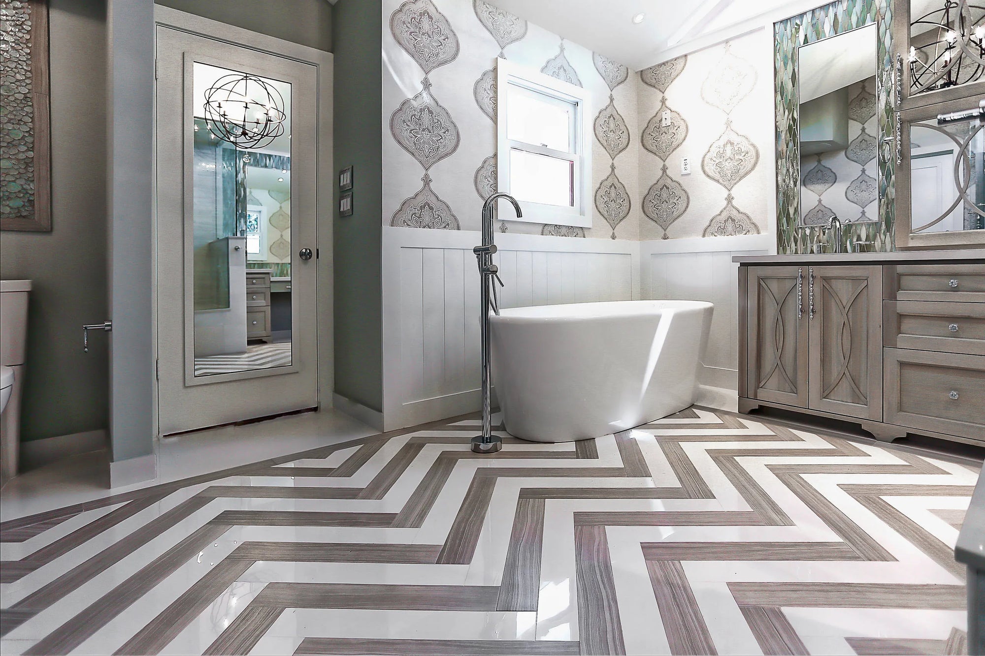 Freestanding bathtub in elegant bathroom with over door mirror, chevron tile floor, and green accent walls.