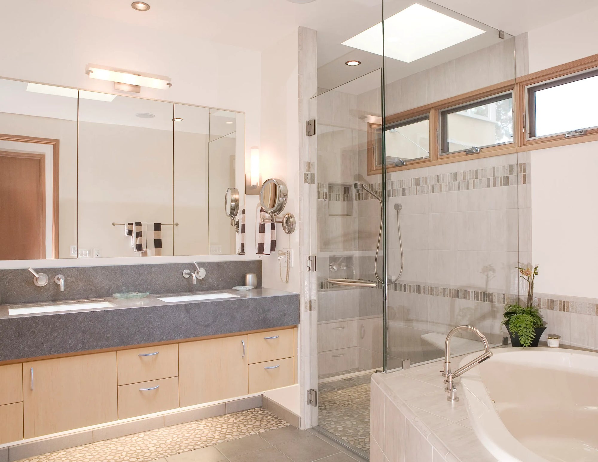 Modern bathroom with a frameless shower enclosure, double vanity, freestanding tub, and natural light through rectangular windows.