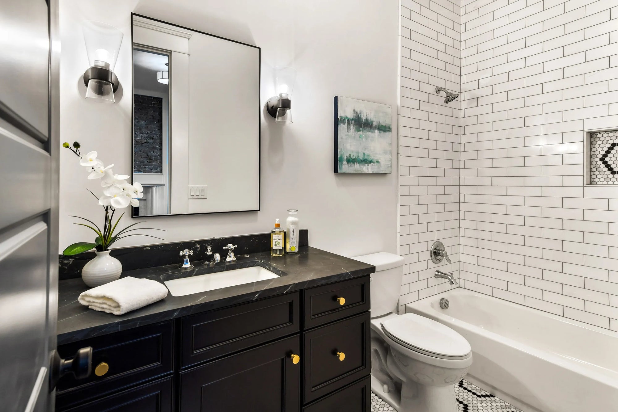 Sleek black bathroom cabinet with gold knobs, white countertop, and a large mirror in an elegant modern bathroom with a neutral color palette.