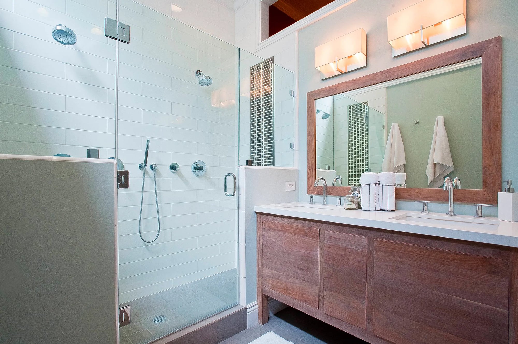 Modern bathroom with glass shower enclosure, subway tiles, chrome shower valve trim, and double vanity.