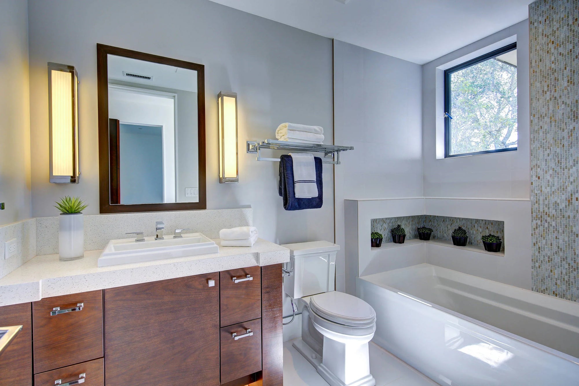 Modern bathroom featuring a drop-in sink set in a light vanity with wood cabinets, a backlit mirror, and a alcove tub